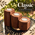 Three-piece American Brown wooden tea light candle holder set with unscented white tea lights, arranged in graduated sizes on a black outdoor table, with a soft green and gold background and Classic Unscented Tea Light Candle Set text.
